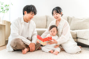 A family sits on a light rug reading a colorful book to their baby on the floor at home.